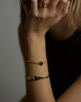 A portrait of a woman holding her face with her hand. On the finger there is the aura ring with natural topaz gemstones. On the wrist there is the cosmos bracelet with natural black onyx gemstone and the ascension cuff with natural black onyx gemstone. All jewelry are made of silver and gold vermeil. Demi-fine jewelry. Made in Athens, Greece, Europe,EU.