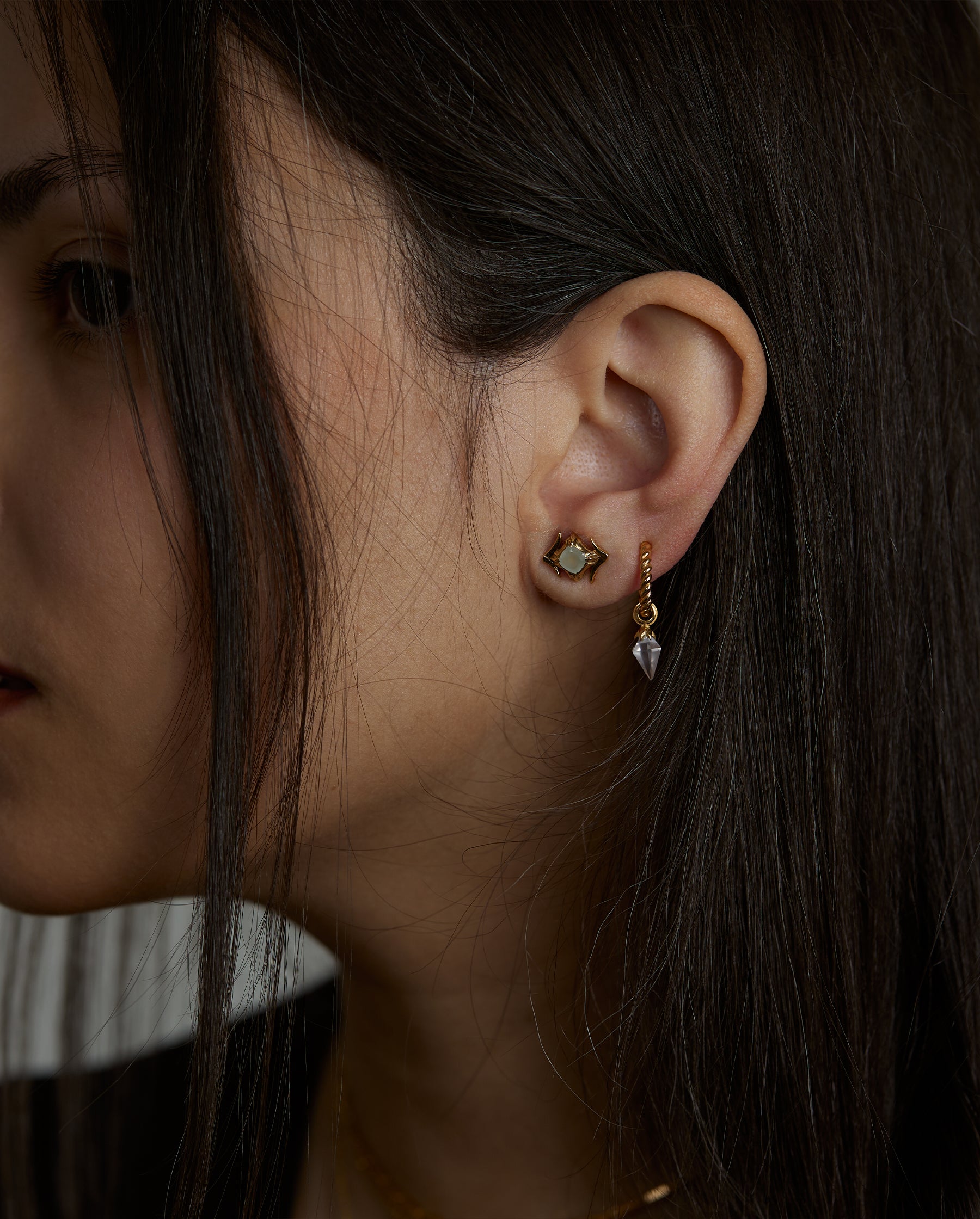 A closeup of the ear of a woman who wears two earrings. The essence hoop earring with natural rose quartz gemstone and the ascension stud earring with natural aquamarine gemstone. All jewelry are made of silver and gold vermeil. Demi-fine jewelry. Made in Athens, Greece, Europe,EU.