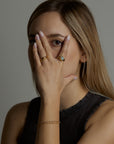 A portrait of a woman model covering her face with her hand. On her hand she is wearing the light and shadow rings with topaz natural gemstones and the ascension ring with natural aquamarine gemstone. On her wrist she wears the hearts double chain labradorite bracelet. All jewelry are made of silver and gold vermeil. Demi-fine jewelry. Made in Athens, Greece, Europe,EU.