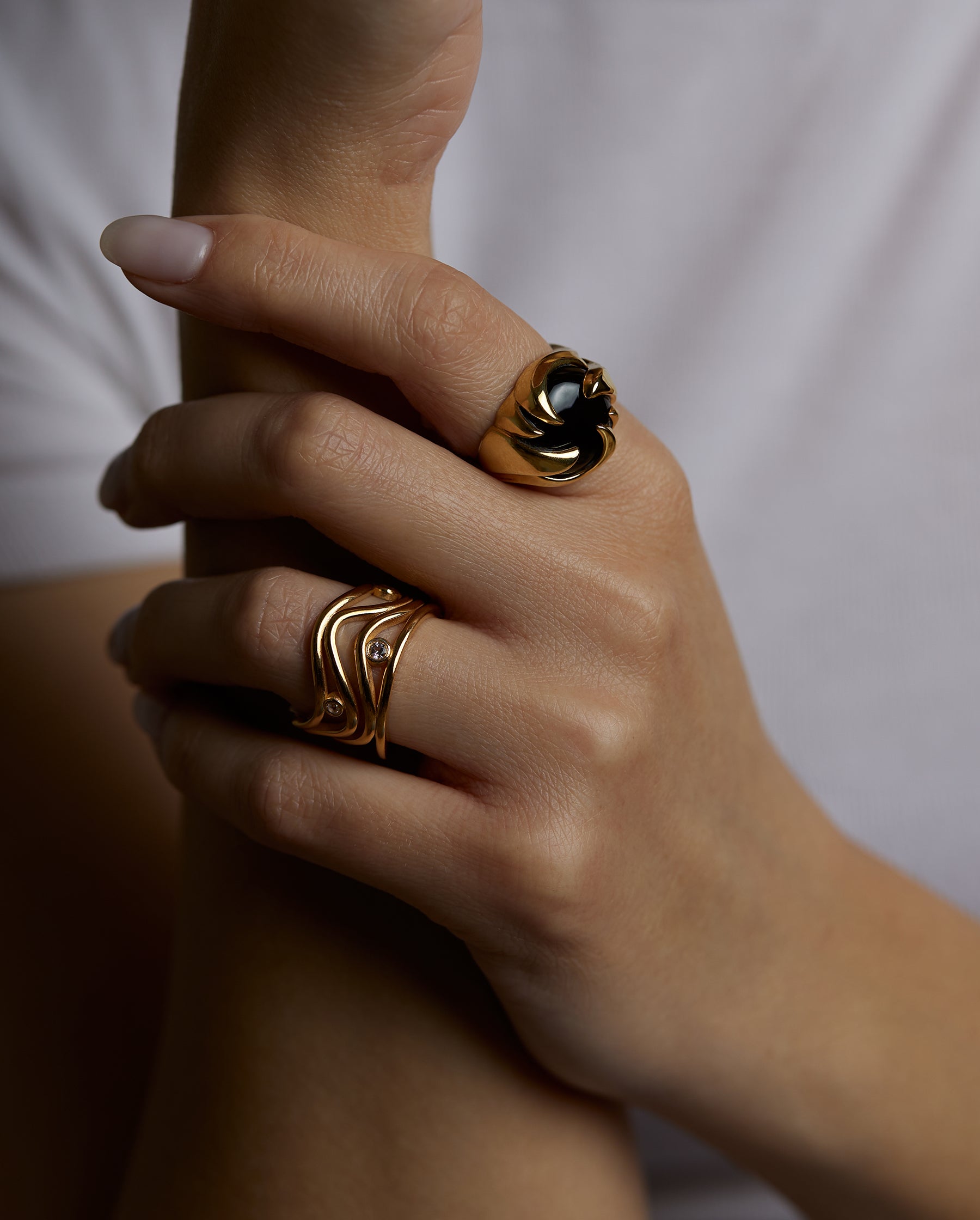 A closeup of a hand with two rings. The cosmos statement ring with natural black onyx gemstone and the aura ring with multiple natural topaz gemstones. All jewelry are made of silver and gold vermeil. Demi-fine jewelry. Made in Athens, Greece, Europe,EU.