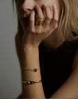 A portrait of a woman holding her face with her hand. On the finger she wears the aura ring with natural topaz gemstones. On the wrist she wears the cosmos bracelet with natural black onyx gemstone and the ascension cuff with natural black onyx gemstone. All jewelry are made of silver and gold vermeil. Demi-fine jewelry. Made in Athens, Greece, Europe,EU.