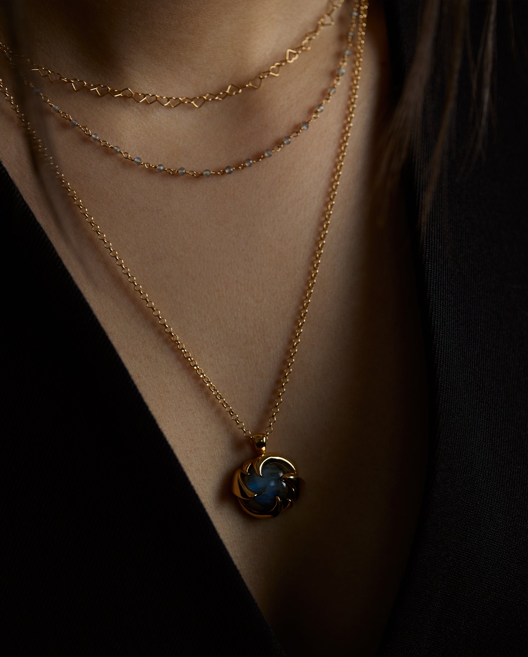 A closeup portrait of a woman model's neck wearing the cosmos pendant with a blue labradorite natural gemstone and the hearts labradorite double chain necklace. All jewelry are made of silver and gold vermeil. Demi-fine jewelry. Made in Athens, Greece, Europe,EU.