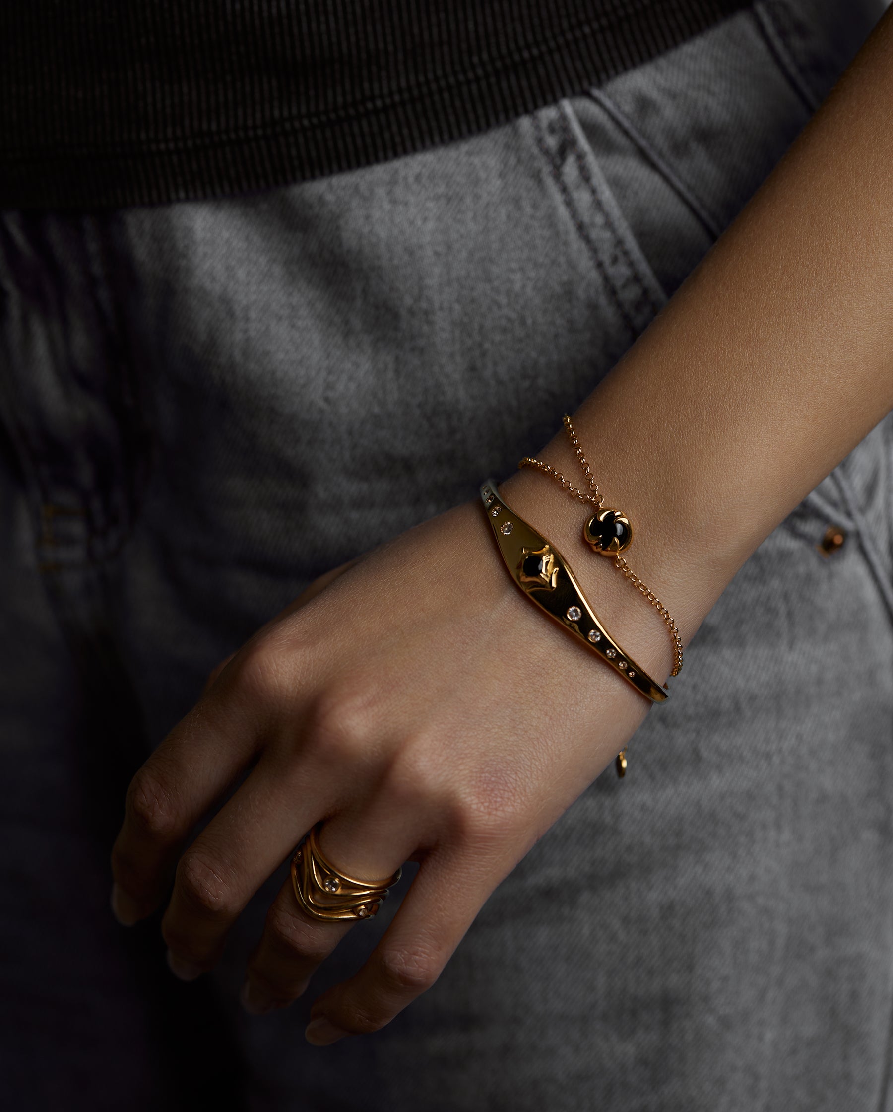 A closeup of a hand with jewelry. On the finger there is the aura ring with natural topaz gemstones. On the wrist there is the cosmos bracelet with natural black onyx gemstone and the ascension cuff with natural black onyx gemstone. All jewelry are made of silver and gold vermeil. Demi-fine jewelry. Made in Athens, Greece, Europe,EU.