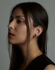 A portrait of a side profile of a woman model that on her ear is wearing two earrings. The cosmos earrings with natural black onyx gemstones and the luck hoop earrings with natural topaz gemstones. All jewelry are made of silver and gold vermeil. Demi-fine jewelry. Made in Athens, Greece, Europe,EU.